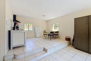A compact kitchen with a sink, stove, and refrigerator, a dining area with a table and chairs, and a large window providing natural light. - Family Chalet by Moncontour Lake (Moncontour)