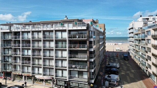 Ein mehrstöckiges Hotel mit Balkonen, Blick auf den Strand und einem Parkplatz.