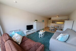 A living room with a brown sofa, a grey sofa, a TV, a small table with a plant, and a kitchen area in the background. - Central Coastal Apartment for 4 (OOSTDUINKERKE)