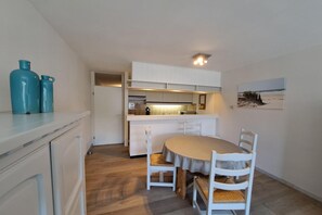 A compact kitchen with white cabinets, a dining table with chairs, and a small island. - Central Coastal Apartment for 4 (OOSTDUINKERKE)