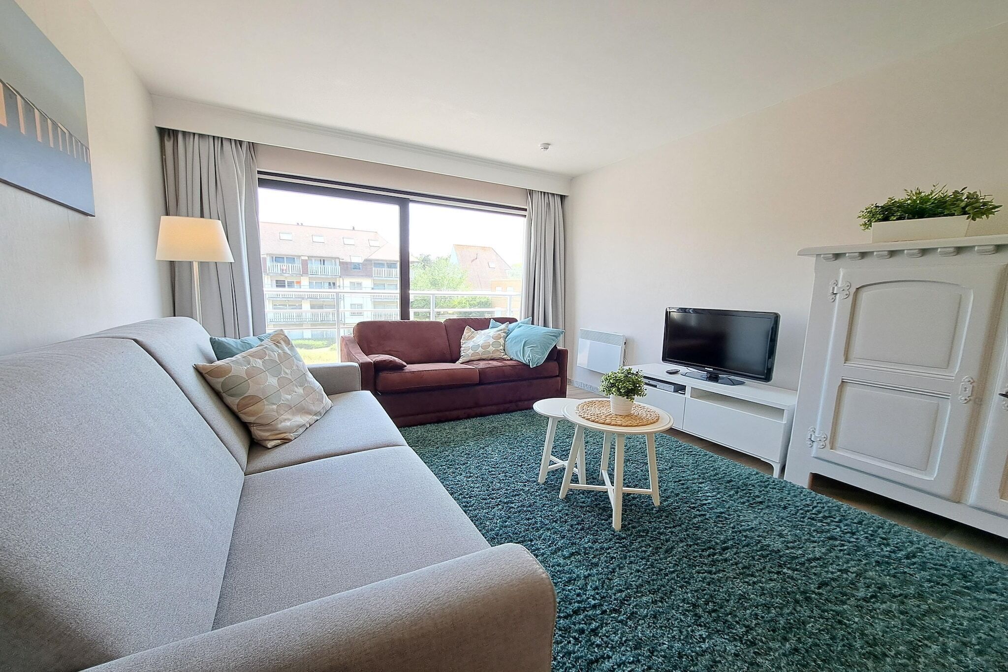 A modern living room with a sofa, a brown armchair, a television, and a cabinet.