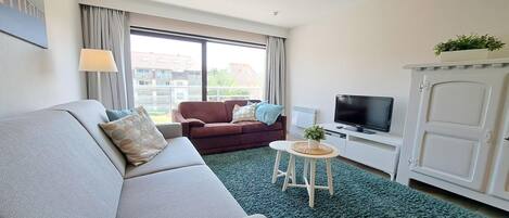 A modern living room with a sofa, a brown armchair, a television, and a cabinet.