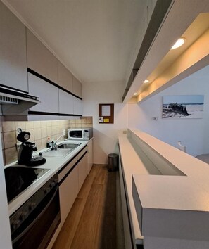 A narrow kitchen with a microwave, stove, and sink. - Central Coastal Apartment for 4 (OOSTDUINKERKE)