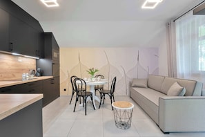 A modern kitchen with dark cabinets, a wooden countertop, a dining table with chairs, and a round coffee table with a woven base. - Stylish Apartment with a Balcony | Parking (Szklarska Poręba)
