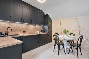 A modern kitchen with dark cabinets, a wooden countertop, and a dining area with a round table and chairs. - Stylish Apartment with a Balcony | Parking (Szklarska Poręba)