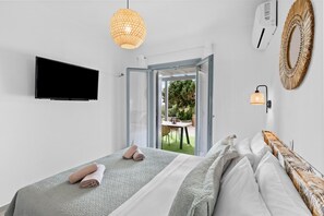 Ein Schlafzimmer mit zwei Betten, einem Fernseher, einer Hängelampe und einer offenen Tür zu einer Terrasse.