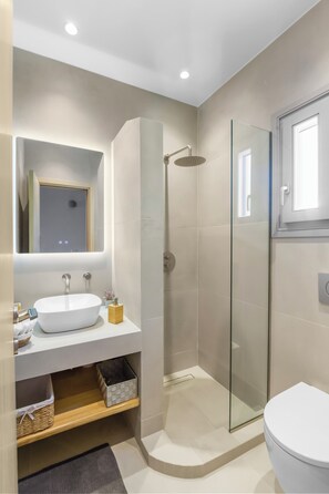 Ein modernes Badezimmer mit einer Glaskabine zur Dusche, einem weißen Waschbecken und einem großen Spiegel.