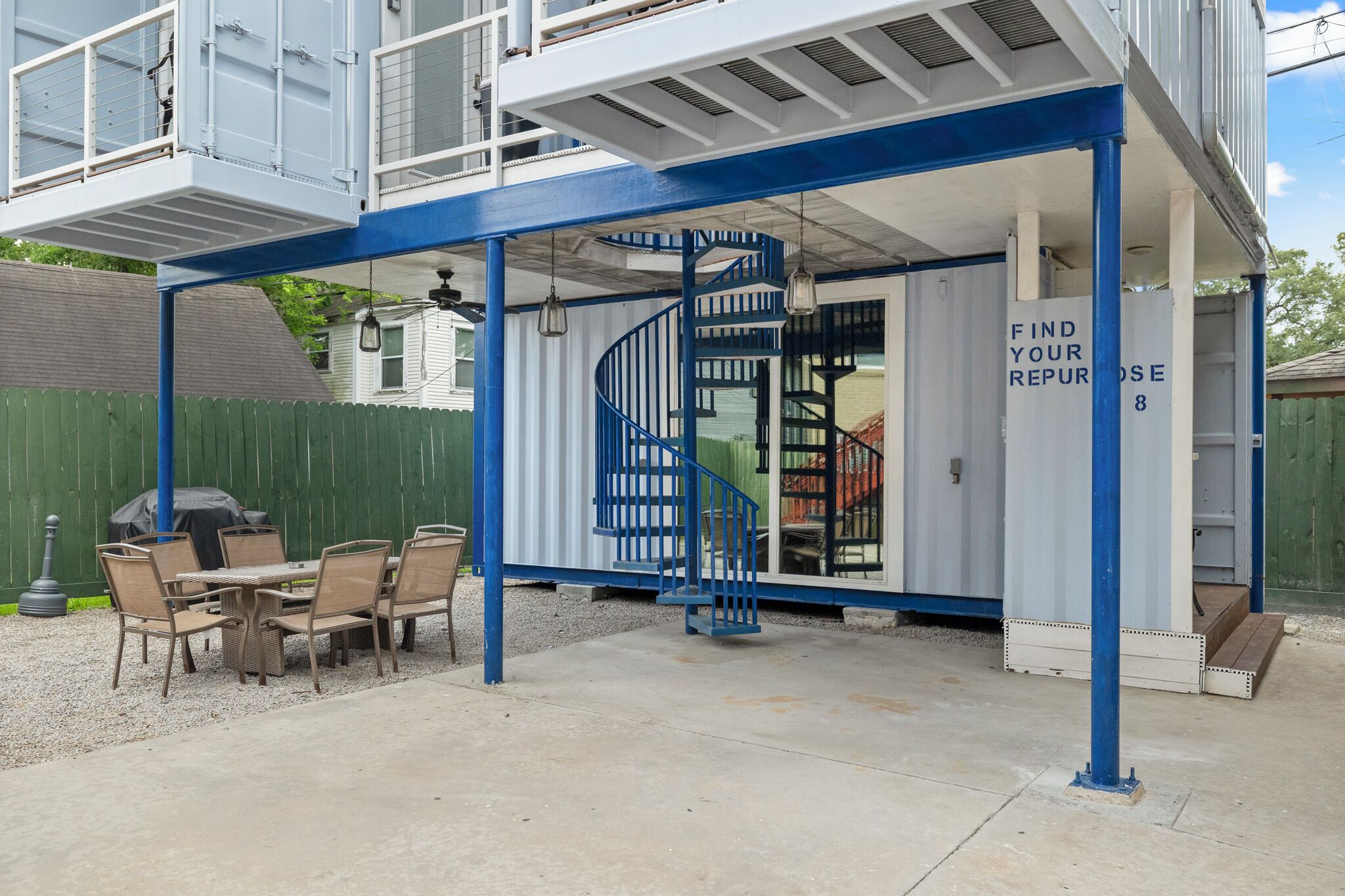 A covered outdoor area with a spiral staircase, a table with chairs, and a sign that reads 'FIND YOUR REPURPOSE.'
