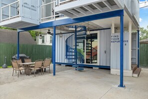 A covered outdoor area with a spiral staircase, a table with chairs, and a sign that reads 'FIND YOUR REPURPOSE.' - Repurposed Living container#8 EADO 2km from FIFA (Houston)