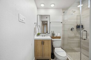 A modern bathroom with a glass shower enclosure, a white sink, and a wooden cabinet. - Repurposed Living container#8 EADO 2km from FIFA (Houston)