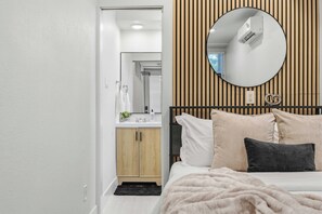 A bedroom with a bed, a round mirror, a wooden headboard, and a small kitchenette. - Repurposed Living container#8 EADO 2km from FIFA (Houston)