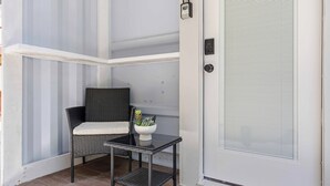 Un rincón con una silla de mimbre, una mesita con una planta y una puerta blanca con cerradura.