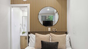 Un dormitorio con cama, un espejo redondo, pared de paneles de madera y una ventana con persianas.