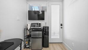 Una kitchenette compacta con microondas, refrigerador, cafetera y un televisor colocado encima del microondas.