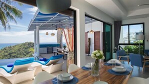 Ein Essbereich mit Meerblick, ein gedeckter Holztisch und Lounge-Sessel mit blauen Kissen.
