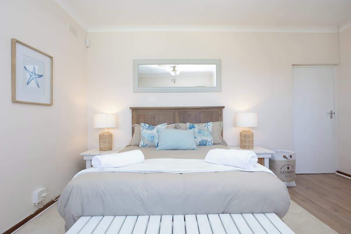A bedroom with a bed, two bedside tables, a nightstand, a mirror, and a framed picture on the wall.