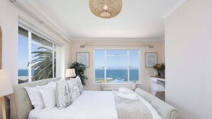 Een slaapkamer met een groot bed, een bureau, een stoel en uitzicht op zee.