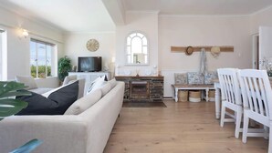 Een woonkamer met een bank, een televisie, een open haard en een eethoek met stoelen.