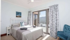 Ein Schlafzimmer mit Bett, Nachttisch, Sessel und Deckenventilator, mit Blick durch eine Glastür.