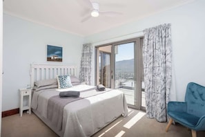 Ein Schlafzimmer mit Bett, Nachttisch, Sessel und Deckenventilator, mit Blick durch eine Glastür.