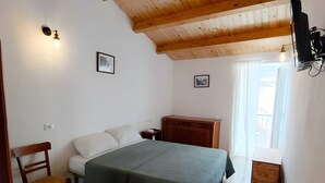 Une chambre avec un plafond en bois, un lit recouvert d’une couverture verte, une chaise, une table de chevet, une commode et un téléviseur fixé au mur.