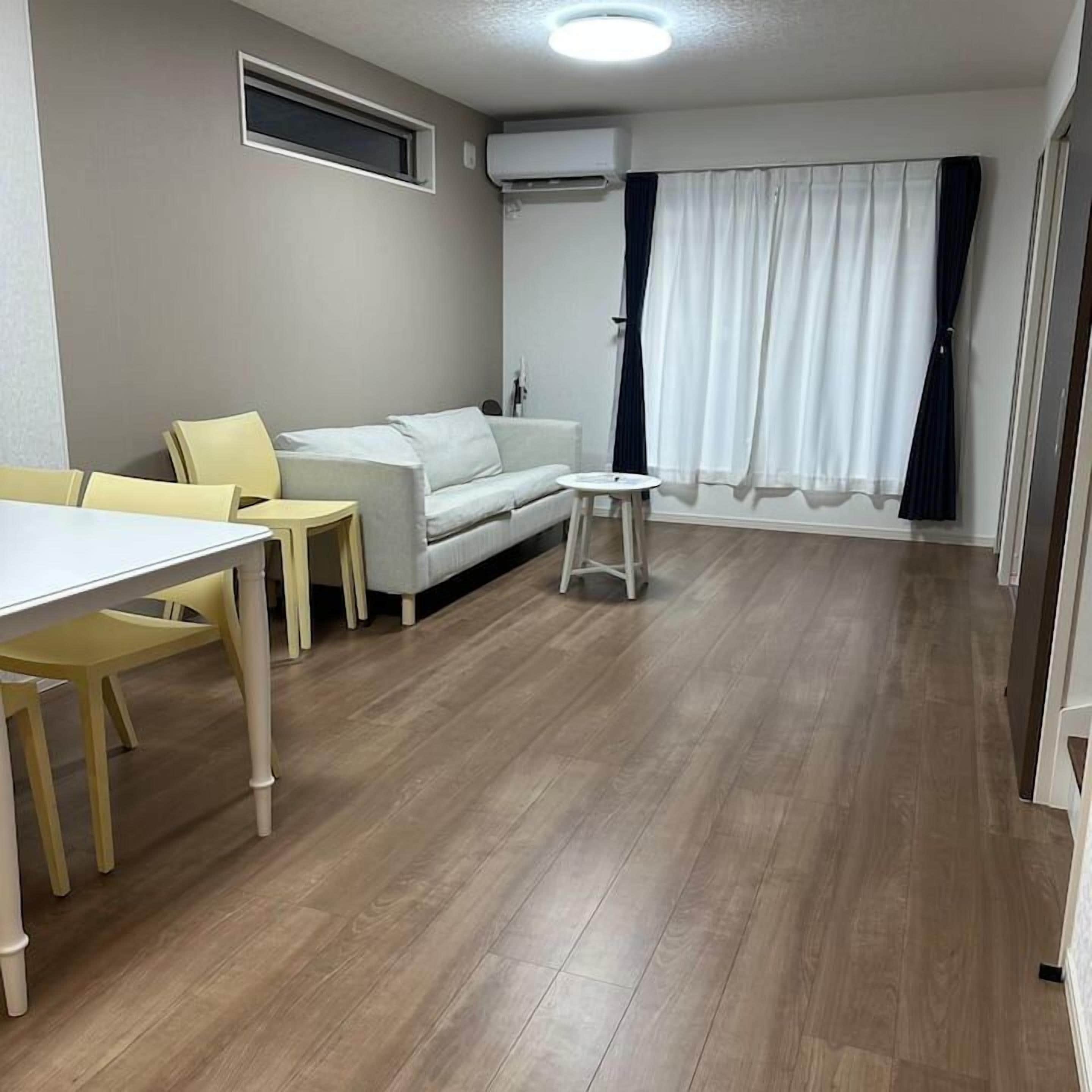 Ein Zimmer mit einem weißen Sofa, gelben Stühlen, einem kleinen weißen Tisch und einem Fenster mit Vorhängen.