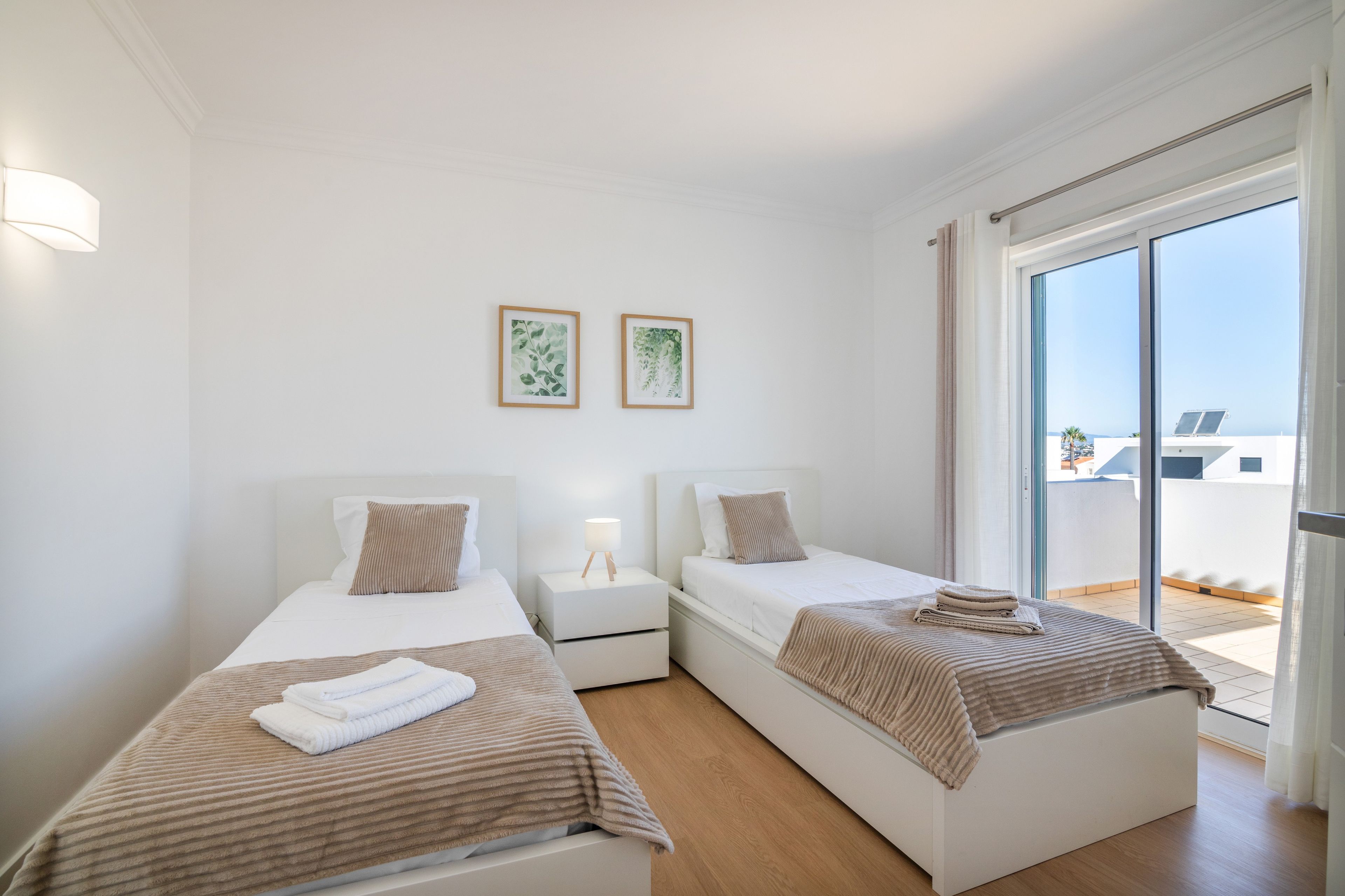 A hotel room with two single beds, a bedside table with a lamp, and a large sliding glass door leading to a balcony.