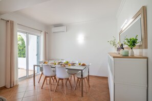 Een eethoek met een tafel gedekt voor vier personen, stoelen, een radiator en een raam met gordijnen.