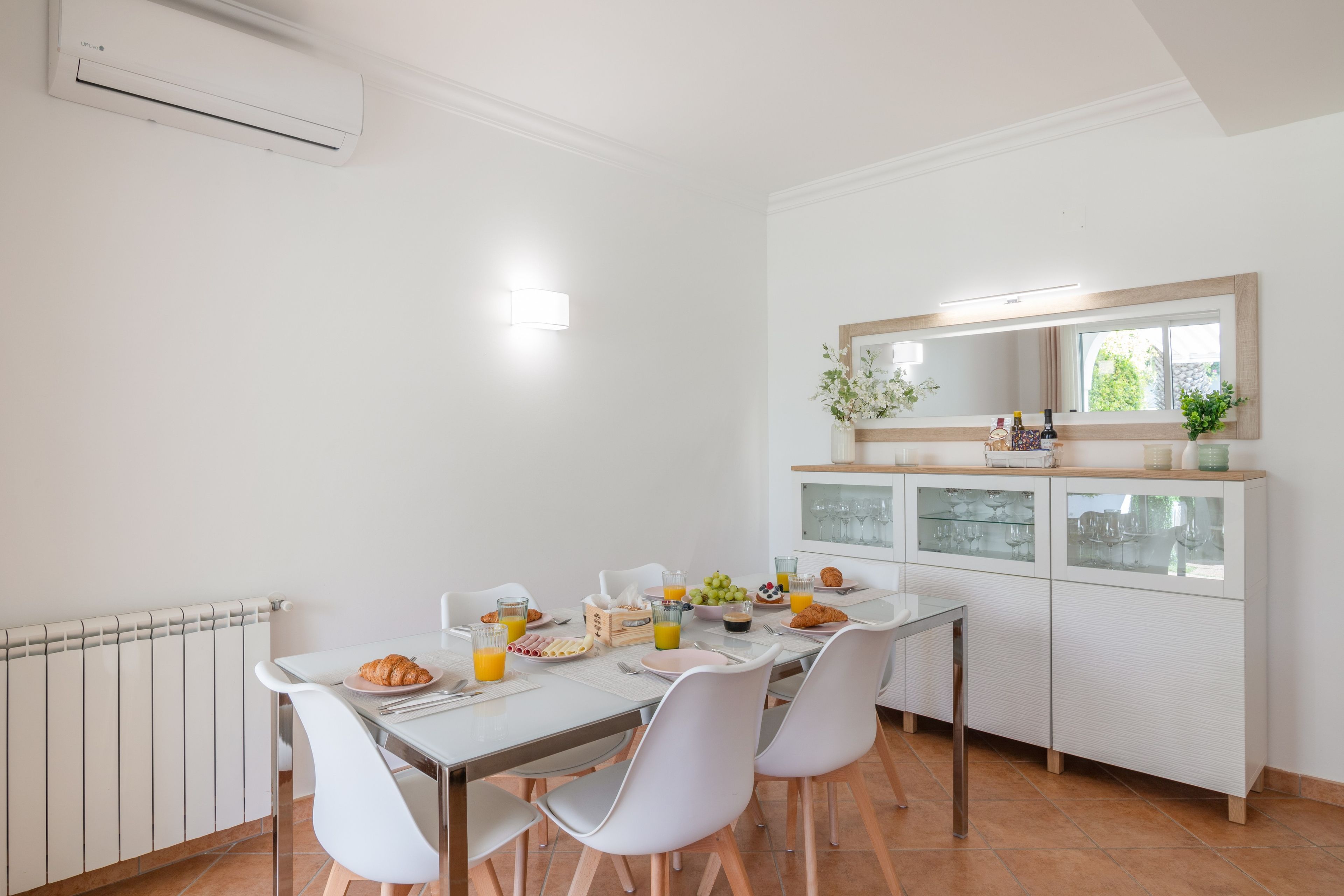 Une cuisine moderne avec une table à manger dressée pour le petit-déjeuner, des chaises blanches et un meuble à vin intégré.