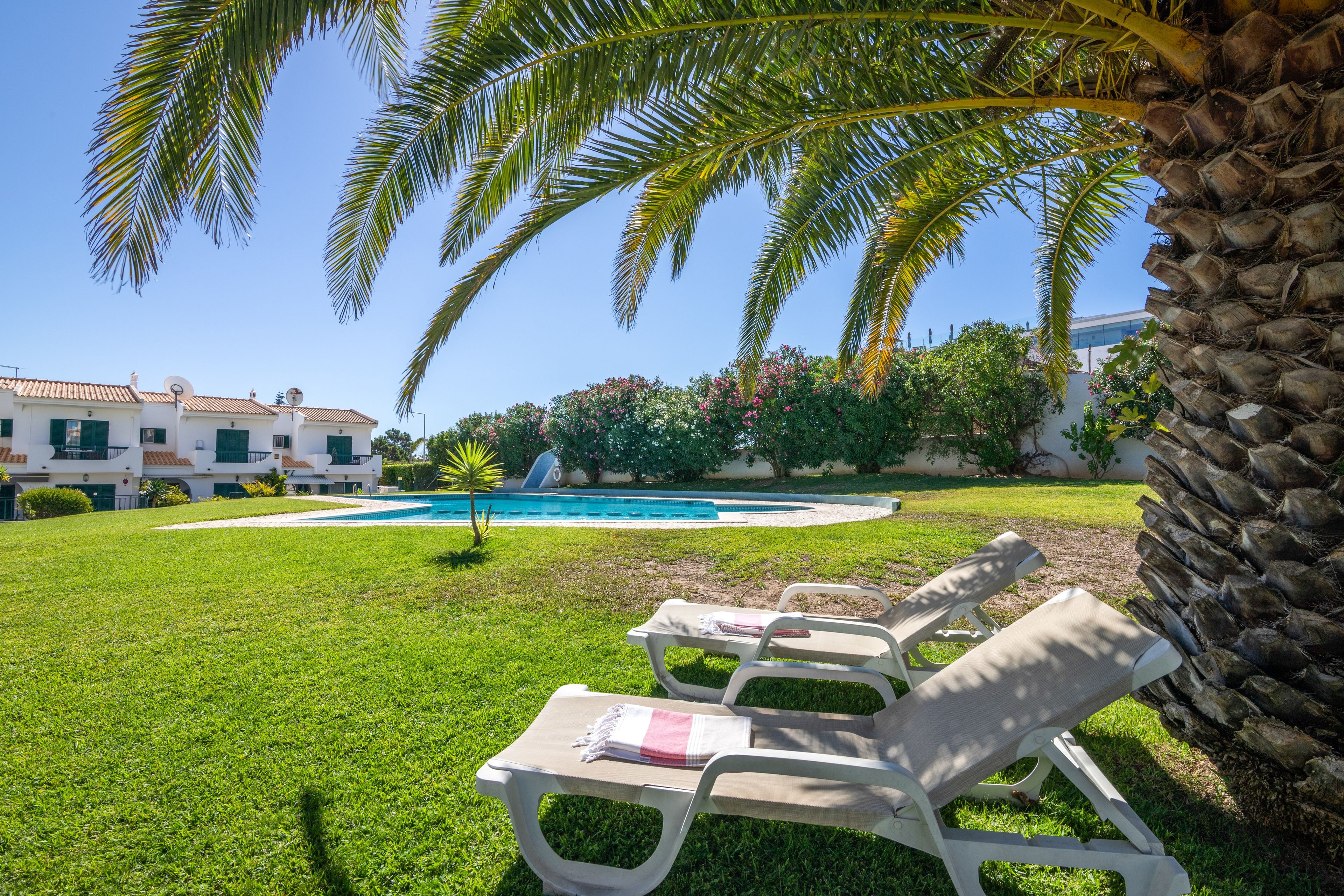 A poolside area with lounge chairs, a swimming pool, and a view of a building with a tiled roof.