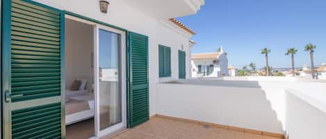 A balcony with a sliding glass door, a tiled floor, and a view of a coastal town.