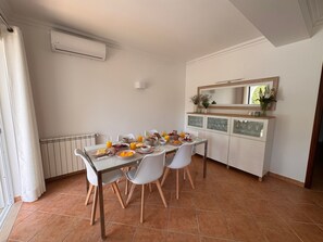 Un comedor con una mesa lista para el desayuno, sillas, un radiador, un equipo de aire acondicionado, un armario con puertas de cristal y un espejo sobre el armario.
