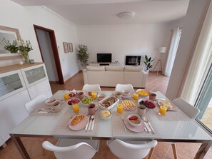 Un coin repas avec une table mise pour le petit-déjeuner, un canapé et un téléviseur en arrière-plan.
