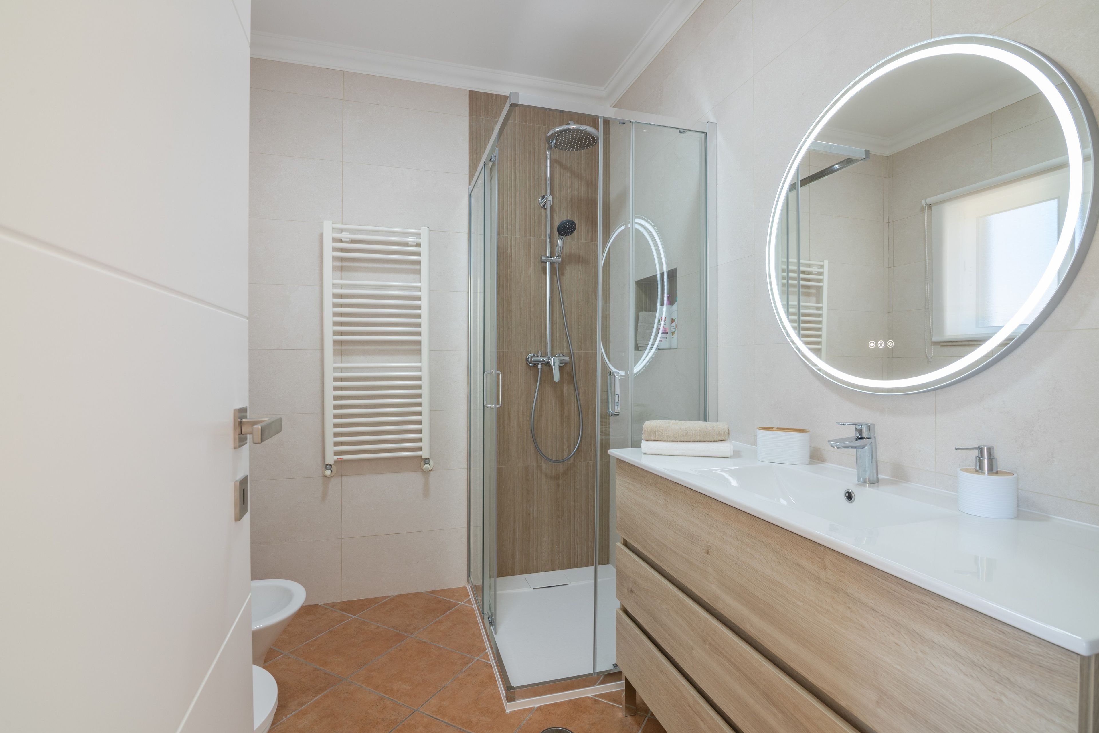 A modern bathroom with a glass-enclosed shower, a toilet, a vanity with a mirror, and a towel dispenser.