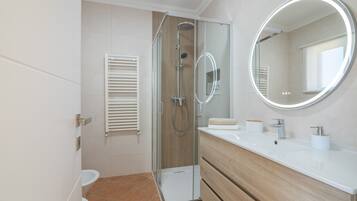 A modern bathroom with a glass-enclosed shower, a toilet, a vanity with a mirror, and a towel dispenser.