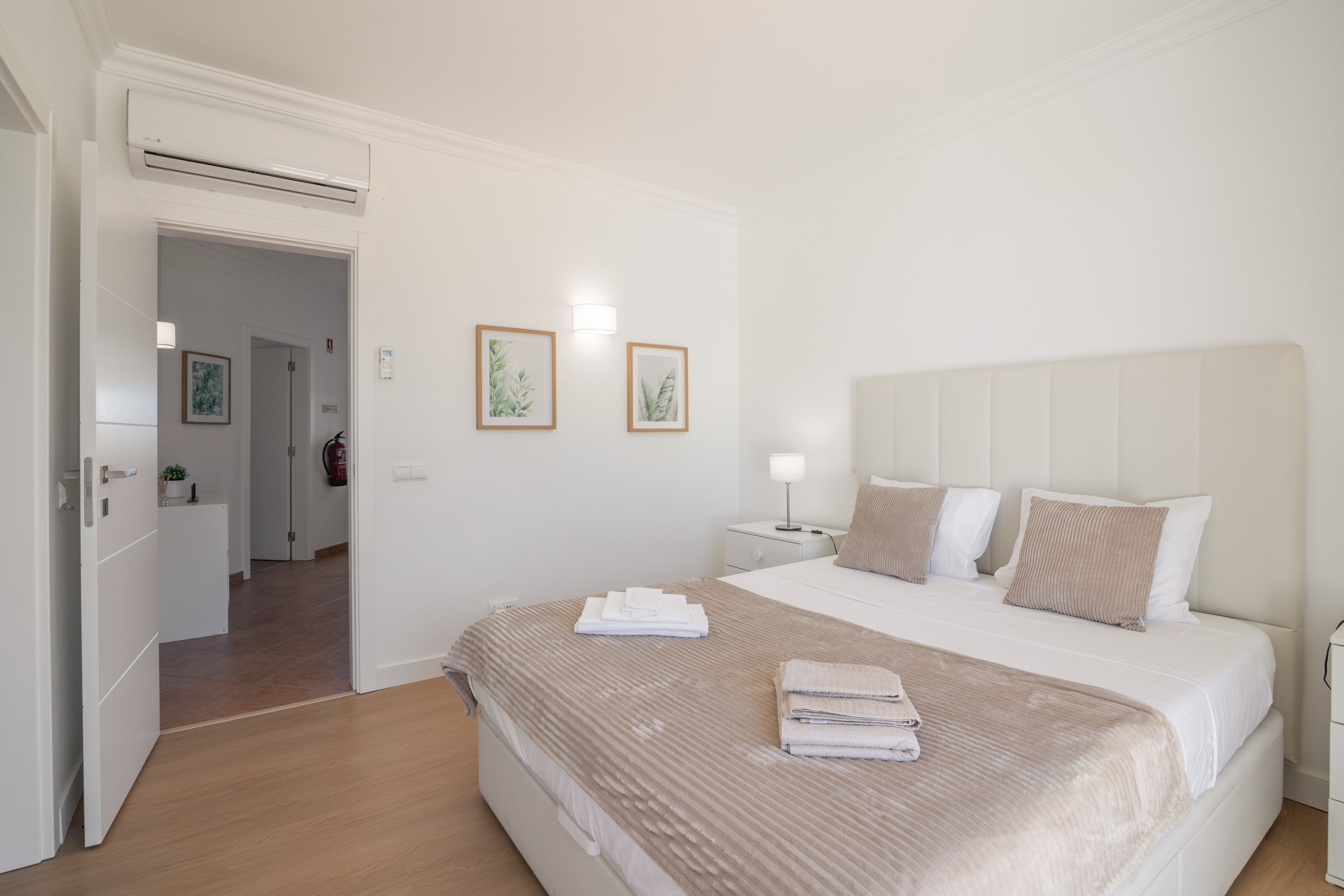 A hotel room with a bed, bedside tables, a nightstand, a wall-mounted light, and a door leading to another room.