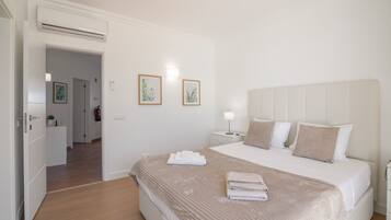 A hotel room with a bed, bedside tables, a nightstand, a wall-mounted light, and a door leading to another room.