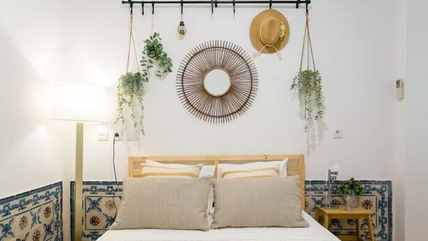 Une chambre à coucher avec un lit, un miroir fixé au mur, des plantes suspendues et un chapeau.