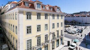 Un immeuble à plusieurs étages, doté d’une façade jaune, de nombreuses fenêtres et d’un toit recouvert de tuiles rouges.