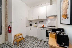 Eine kleine Küche mit weißen Schränken, einem Gasherd, einem Geschirrspüler und einem Toaster.