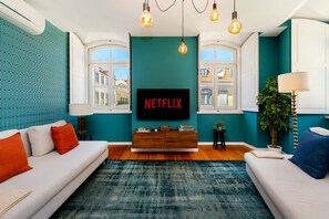 A modern living room with teal walls, a large flat-screen TV, a wooden coffee table, and two sofas with cushions. - Authentic Central Lisbon Gem with Unique Design (Lisboa)
