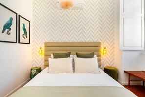 A bedroom with a bed, two wall-mounted lamps, a nightstand, a framed picture, and a window. - Authentic Central Lisbon Gem with Unique Design (Lisboa)
