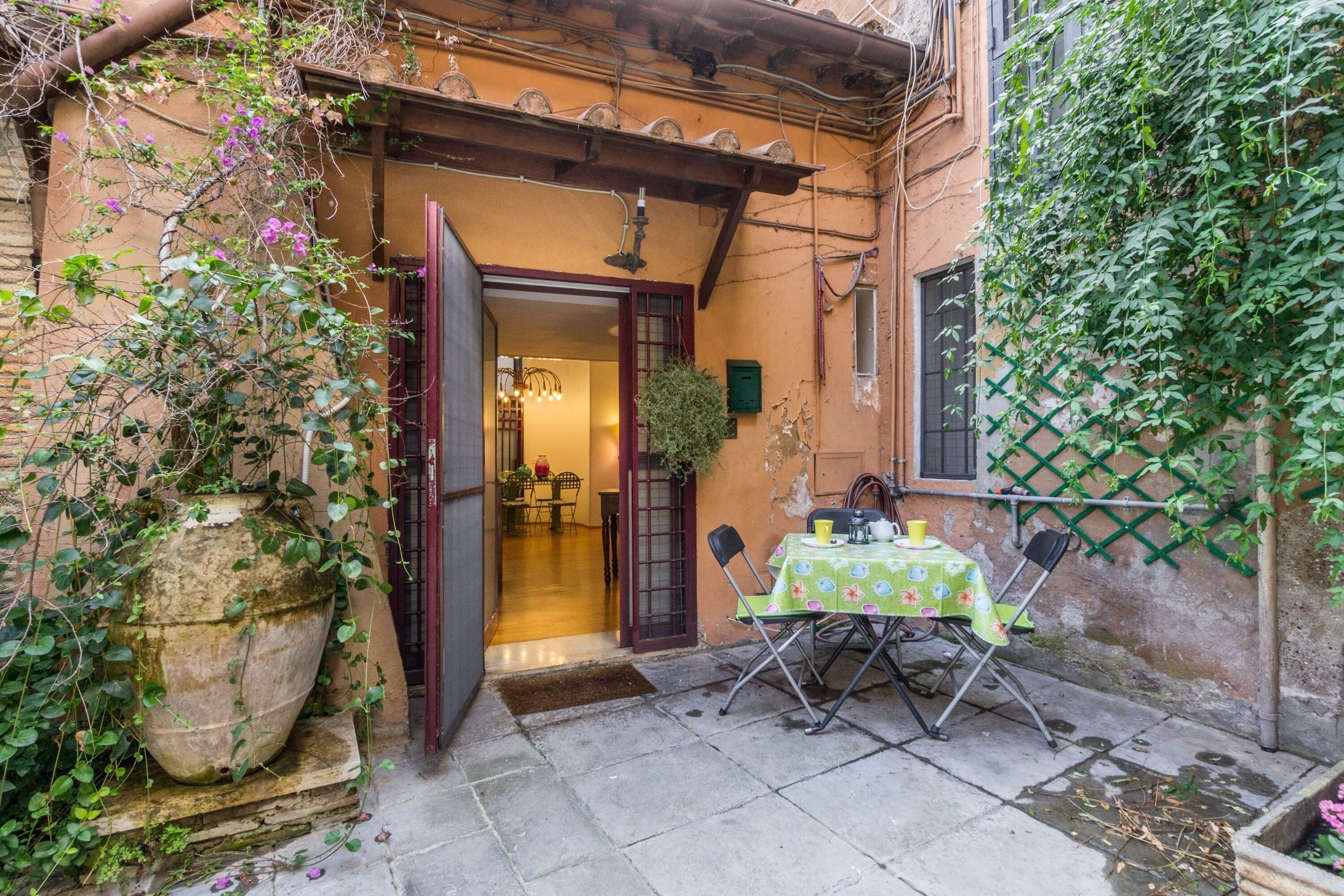 An outdoor patio with a table and chairs, a large potted plant, and a doorway leading to an interior space.