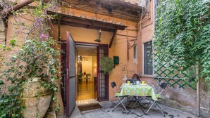An outdoor patio with a table and chairs, a large potted plant, and a doorway leading to an interior space. - Secret Loft in Trastevere - Moro (Rome)
