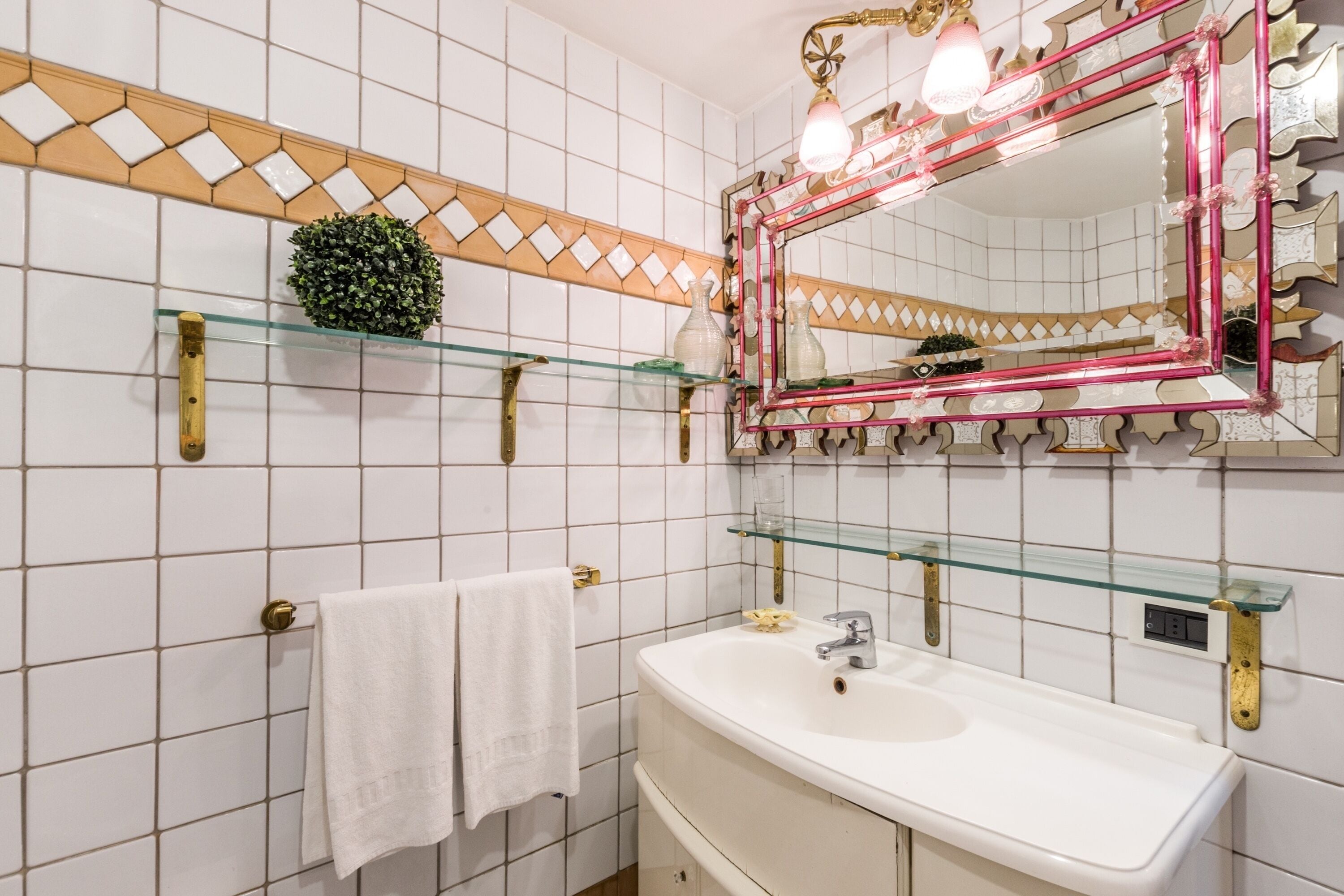 A bathroom with a white sink, a glass shelf, a towel rack, and a decorative mirror with lights.