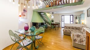 A spacious living area with a glass dining table, green chairs, a sofa, a staircase, and a kitchen area. - Secret Loft in Trastevere - Moro (Rome)
