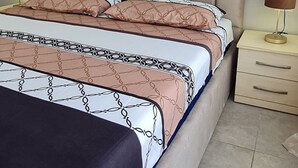 A bed with a patterned bedspread, a headboard, bedside tables with lamps, and a framed picture on the wall. -  A beautiful cozy apartment very close to the beach and to all amenities. (Durrës County)