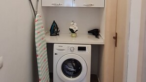 A laundry room with a washing machine, ironing board, and cabinets. -  A beautiful cozy apartment very close to the beach and to all amenities. (Durrës County)