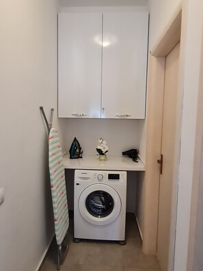A laundry room with a washing machine, ironing board, and cabinets. -  A beautiful cozy apartment very close to the beach and to all amenities. (Durrës County)