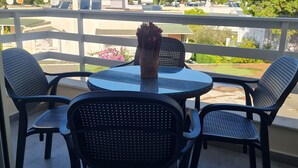 A balcony with a round table and four chairs, a vase with flowers, and a view of buildings and trees. -  A beautiful cozy apartment very close to the beach and to all amenities. (Durrës County)